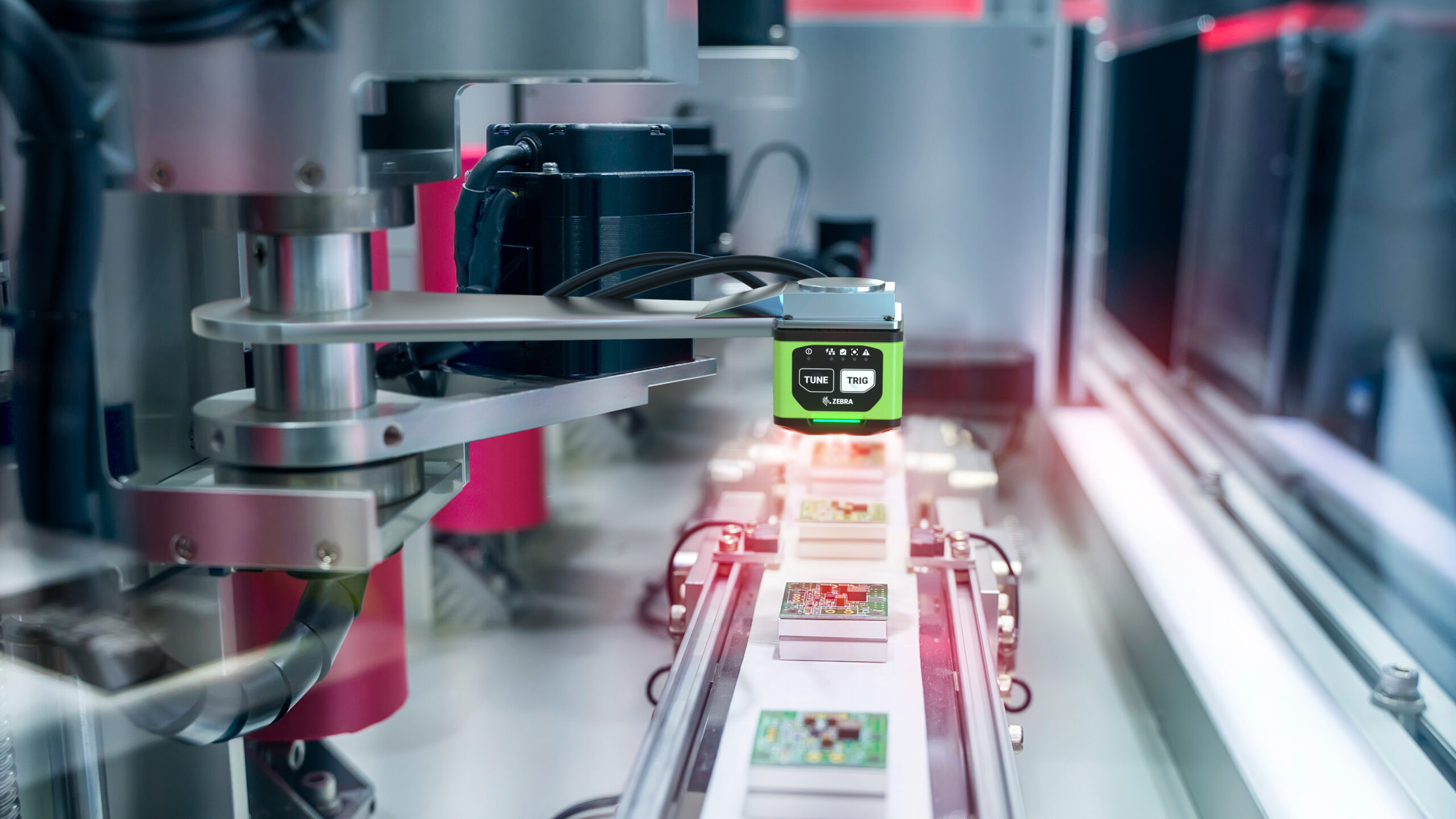 A robotic arm operates on an assembly line, precisely handling small electronic components beneath a bright green sensor, surrounded by modern machinery in a high-tech industrial setting.